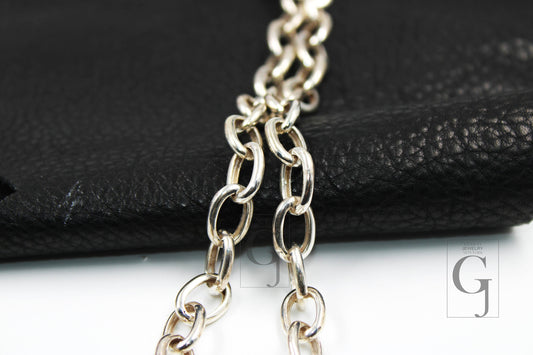 Close-up of a silver white link chain necklace laid out on a black surface.