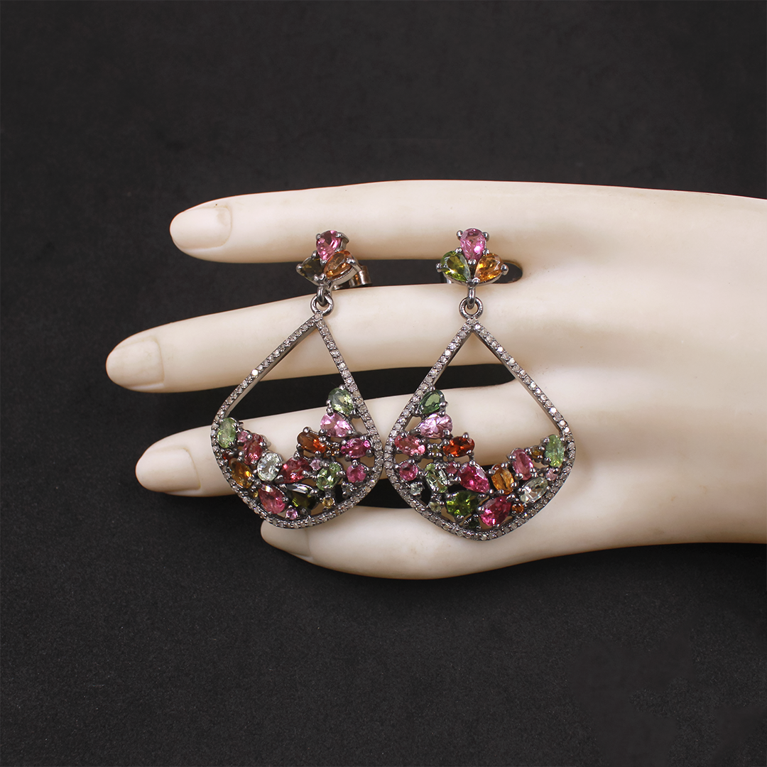 Multicolored gemstone earrings on a mannequin hand against a black background
