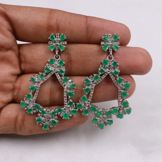 Green gemstone earrings held in a hand against a white background