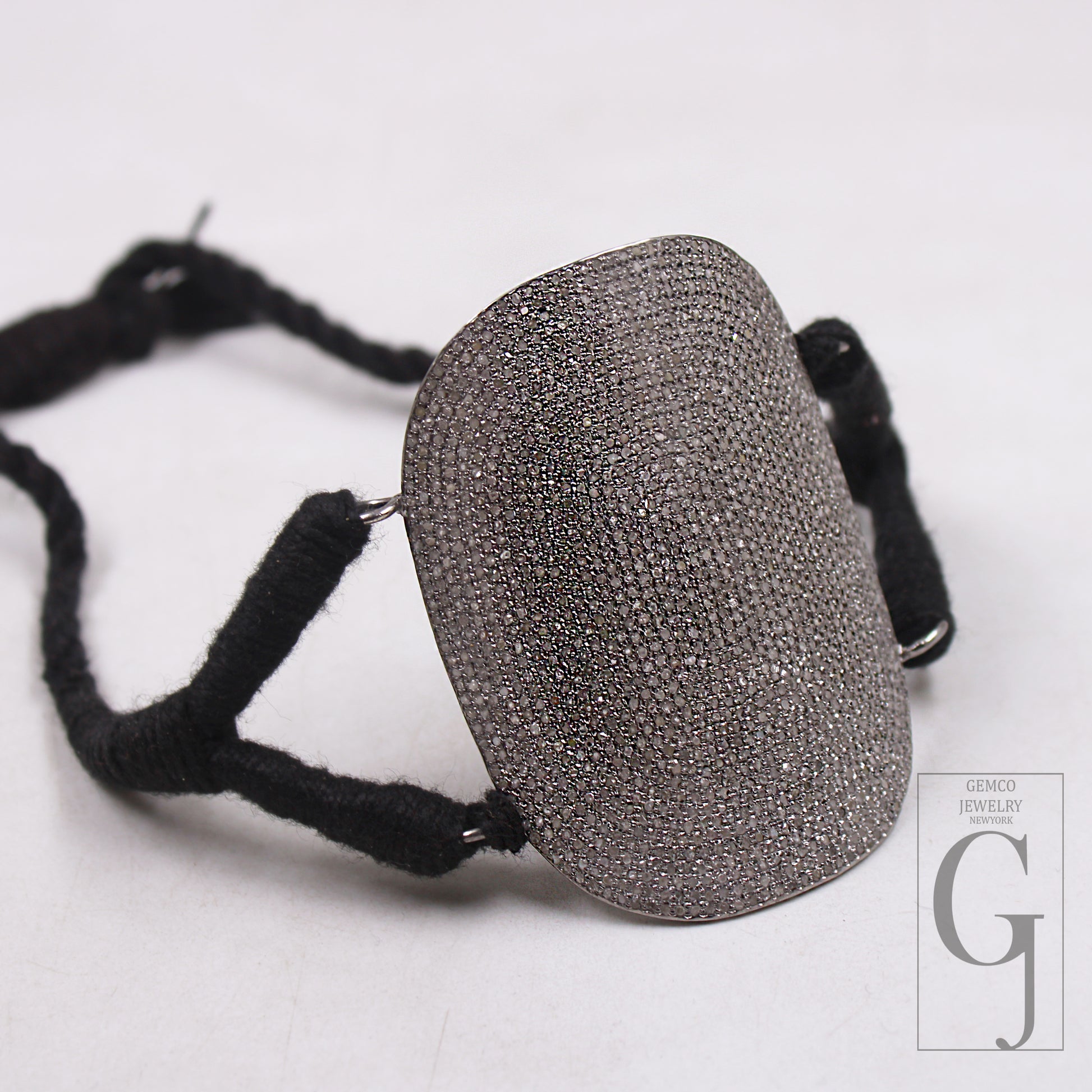 A close-up image of a sterling silver handcrafted bracelet with a rose-cut pave diamond design, featuring a textured surface and attached with black threads.