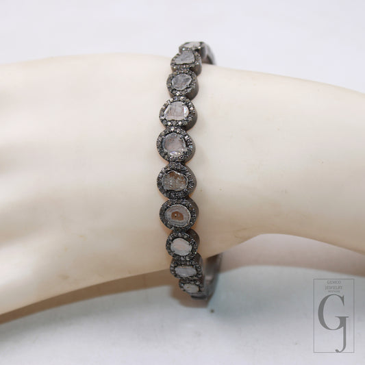 A silver bangle bracelet with a pave diamond finish featuring flat polki diamonds set around a central, larger diamond, displayed on a mannequin wrist.