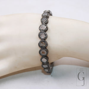 A silver bangle bracelet with a pave diamond finish featuring flat polki diamonds set around a central, larger diamond, displayed on a mannequin wrist.