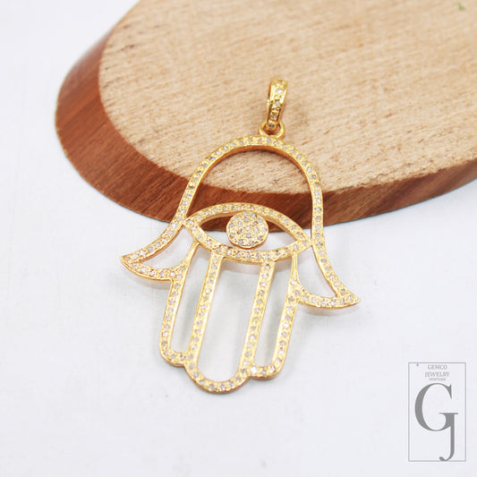 A gold-colored Hamsa Hand pendant with pave diamond detailing on a wooden surface.
