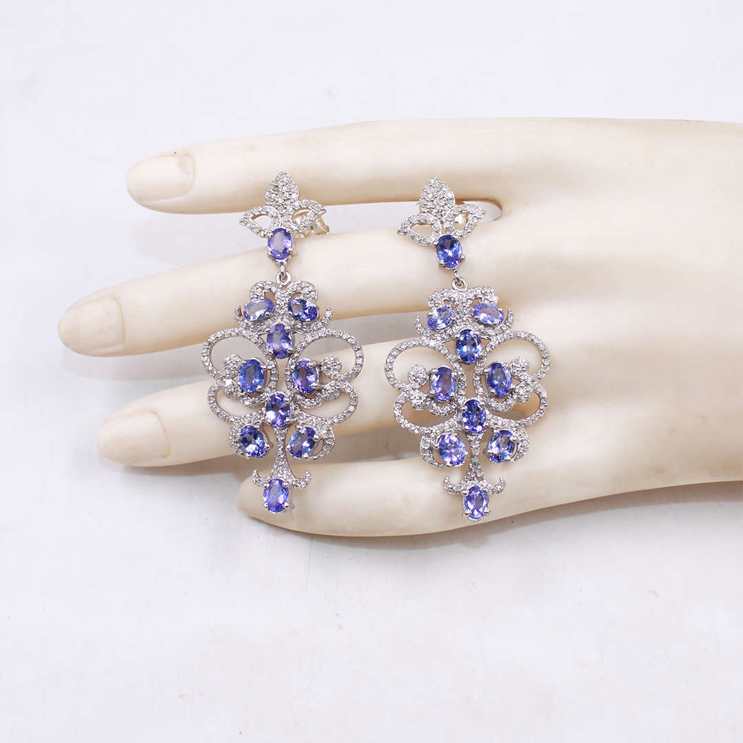 Pair of purple gemstone earrings on a mannequin hand against a white background