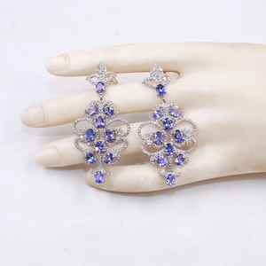 Pair of purple gemstone earrings on a mannequin hand against a white background