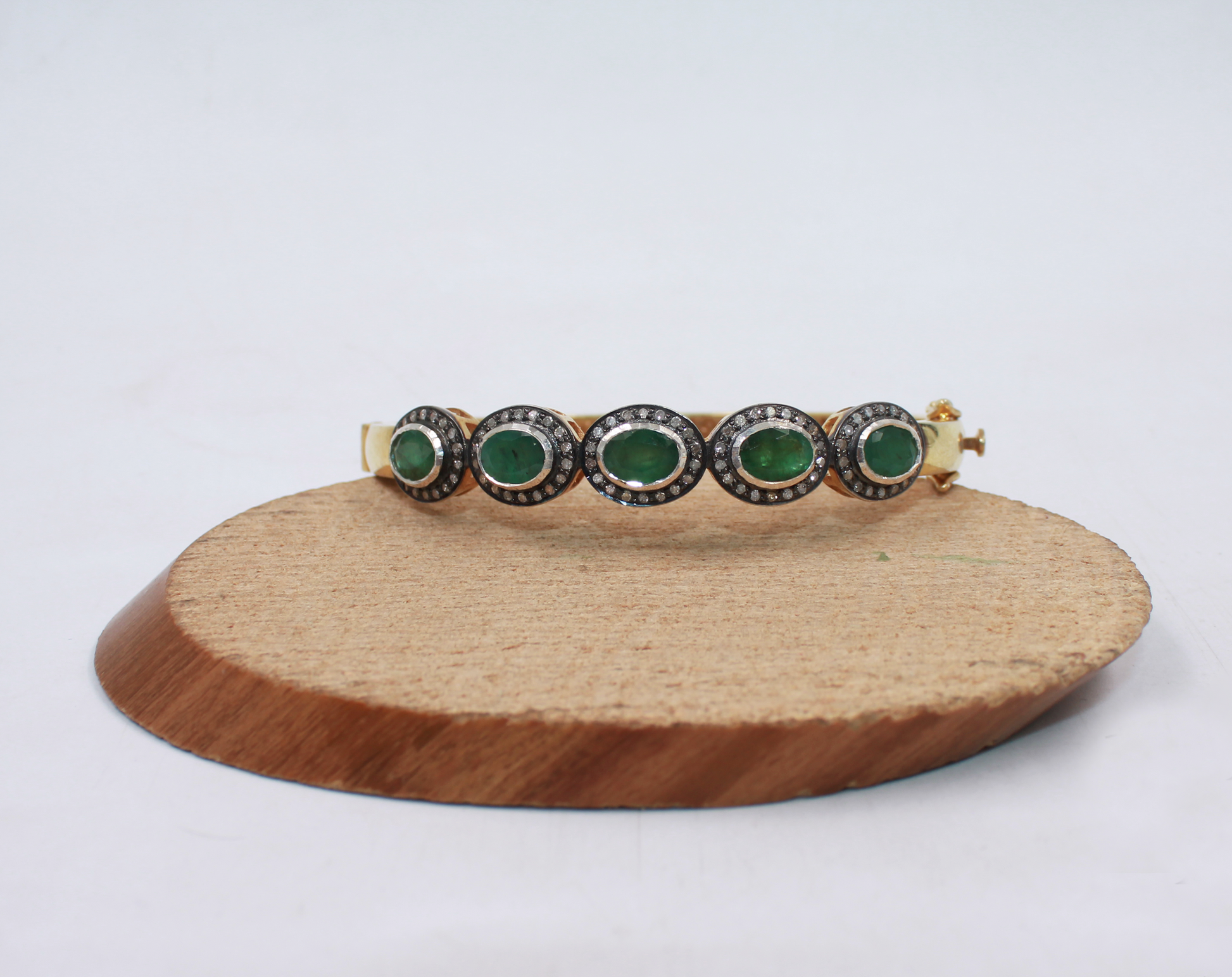 Bracelet with green gemstones on a wooden stand against a white background
