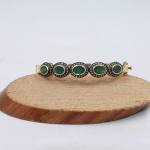 Bracelet with green gemstones on a wooden stand against a white background
