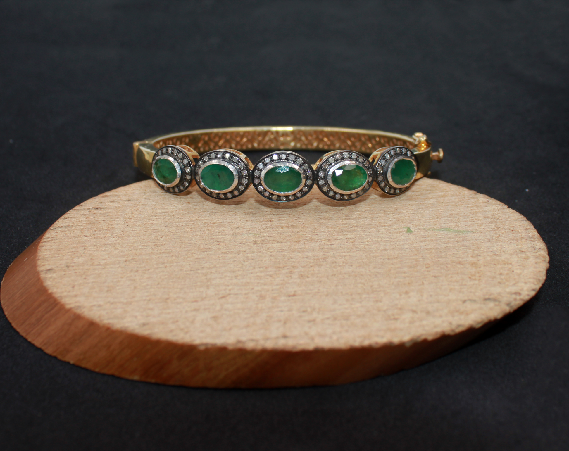Gold bracelet with green gemstones on a wooden stand against a black background