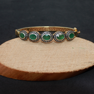 Gold bracelet with green gemstones on a wooden stand against a black background