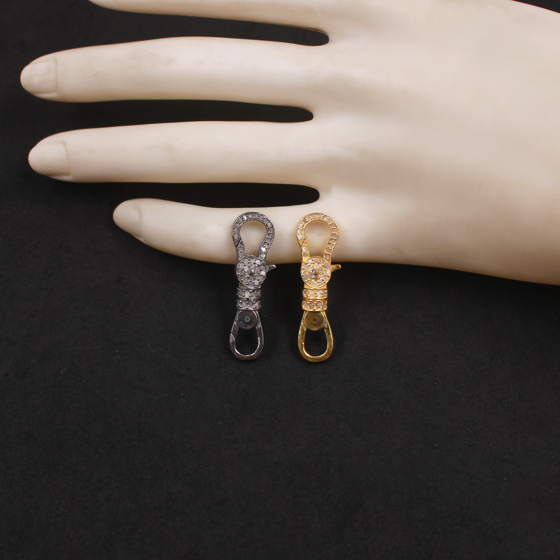 Two metallic keychain clasps, one gold and one silver, on a mannequin hand against a black background.