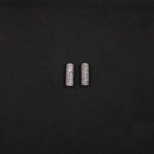 Two silver cylindrical earrings on a black background