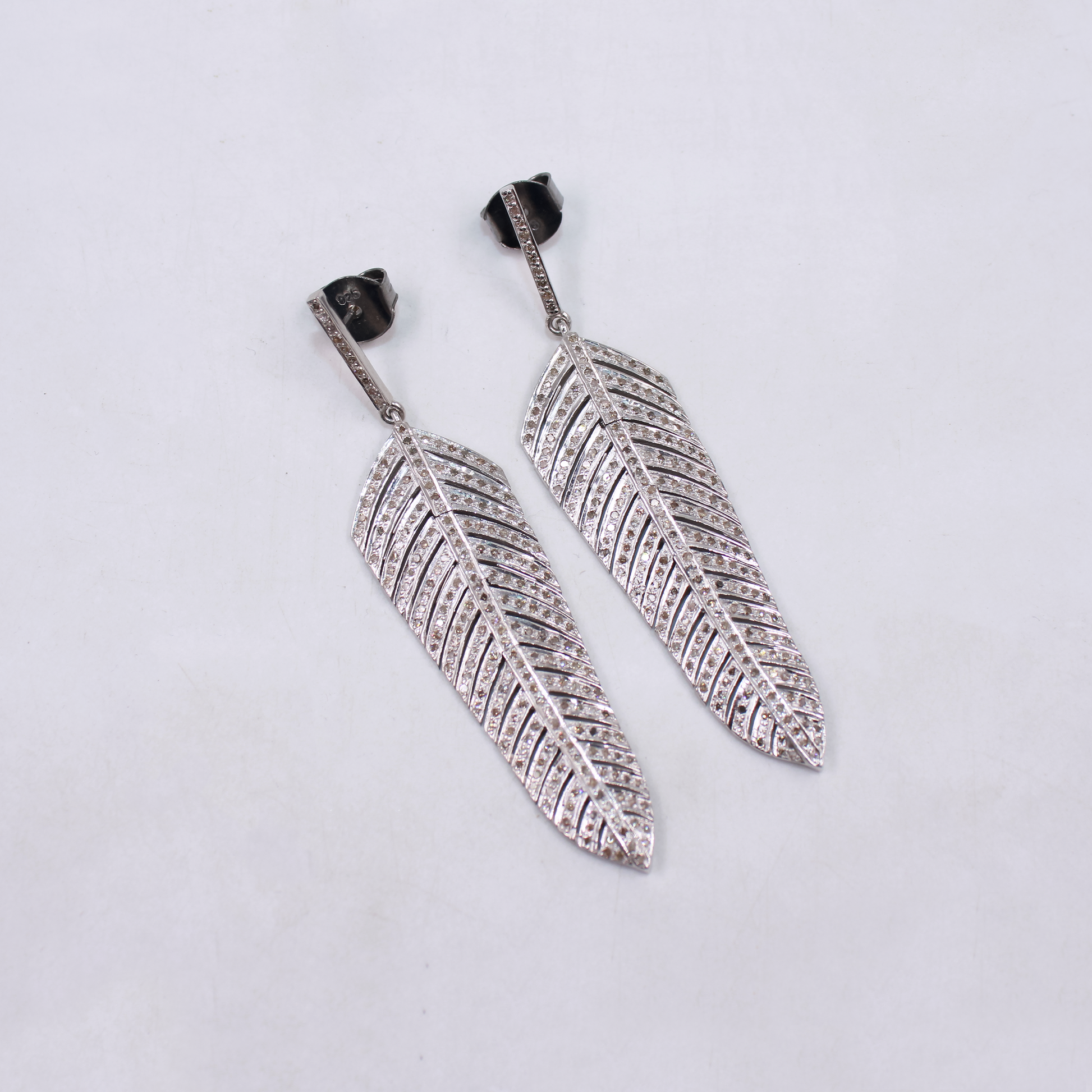 Pair of silver feather-shaped earrings on a light gray background