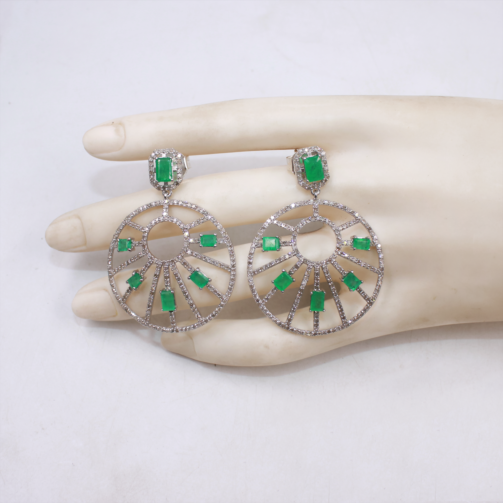 Silver earrings with green gemstones on a mannequin hand against a white background