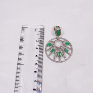 Jewelry pendant with green gemstones and silver accents next to a ruler on a white background