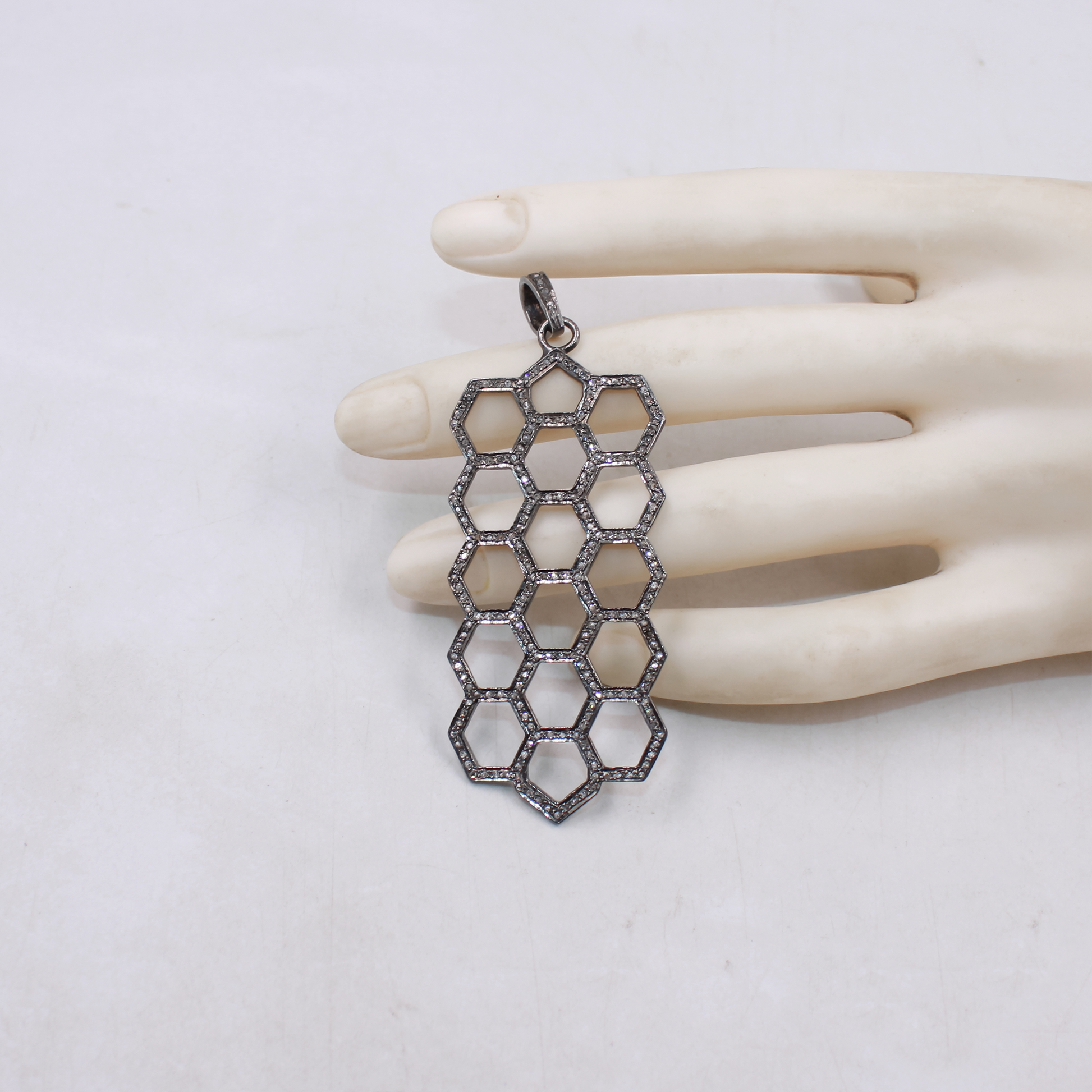 Hexagonal patterned pendant on a mannequin hand against a white background