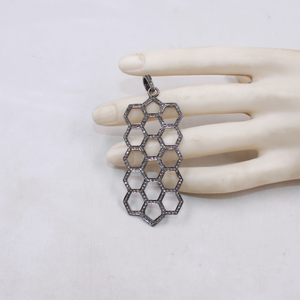 Hexagonal patterned pendant on a mannequin hand against a white background