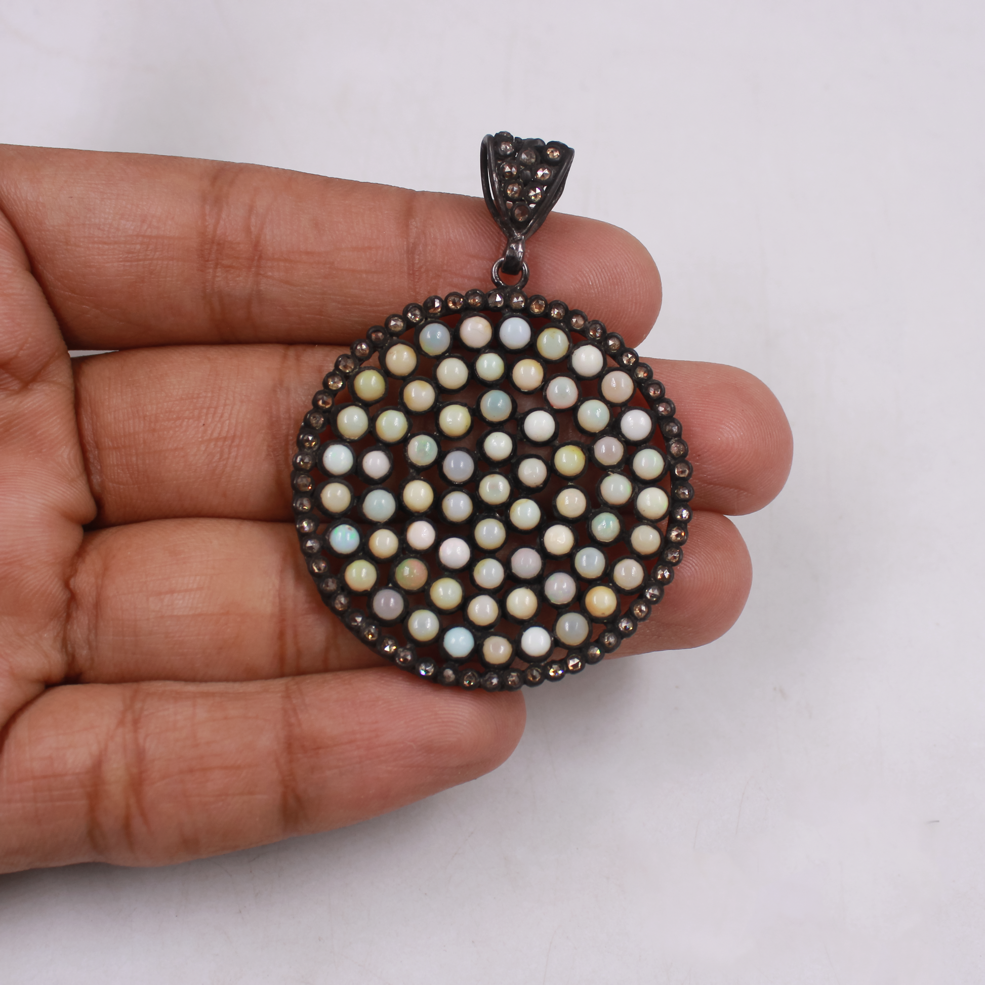 Round pendant with bead-like design held in a hand against a white background