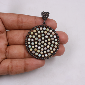 Round pendant with bead-like design held in a hand against a white background