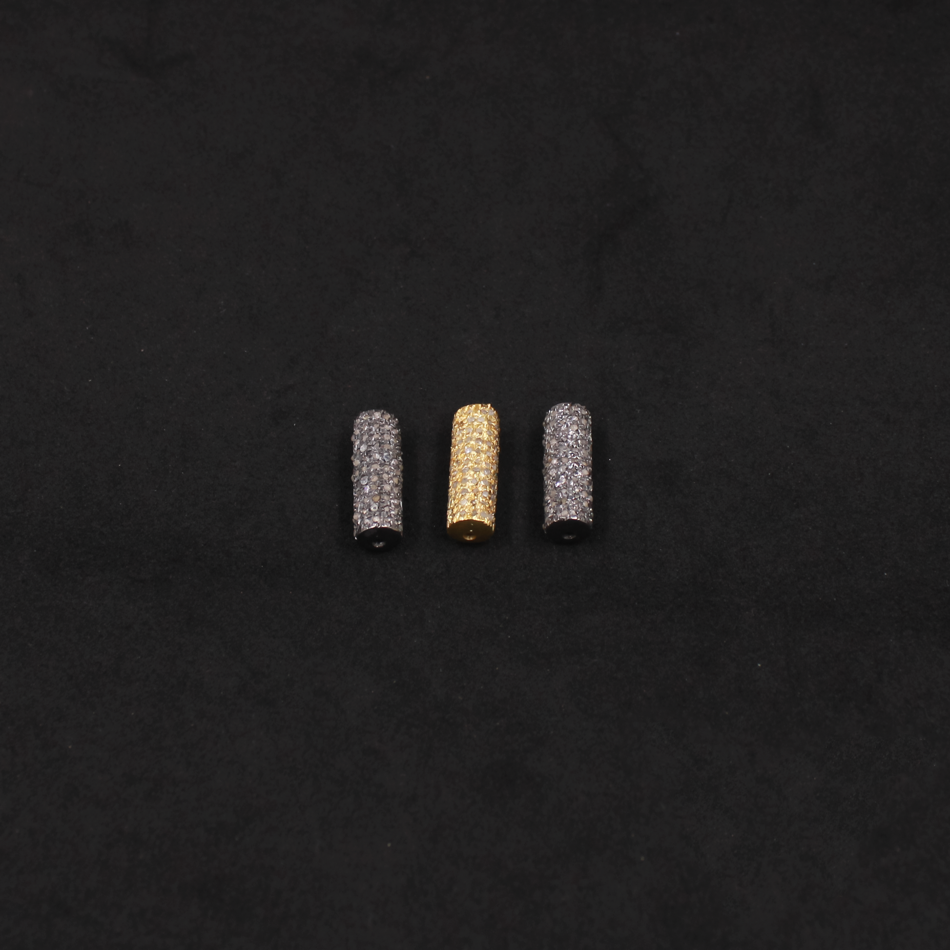 Three cylindrical beads, two silver and one gold, on a black background