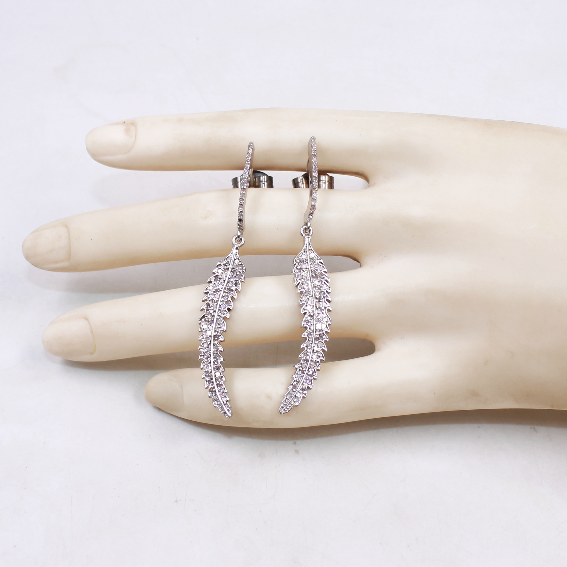 Silver leaf-shaped earrings on a mannequin hand against a white background