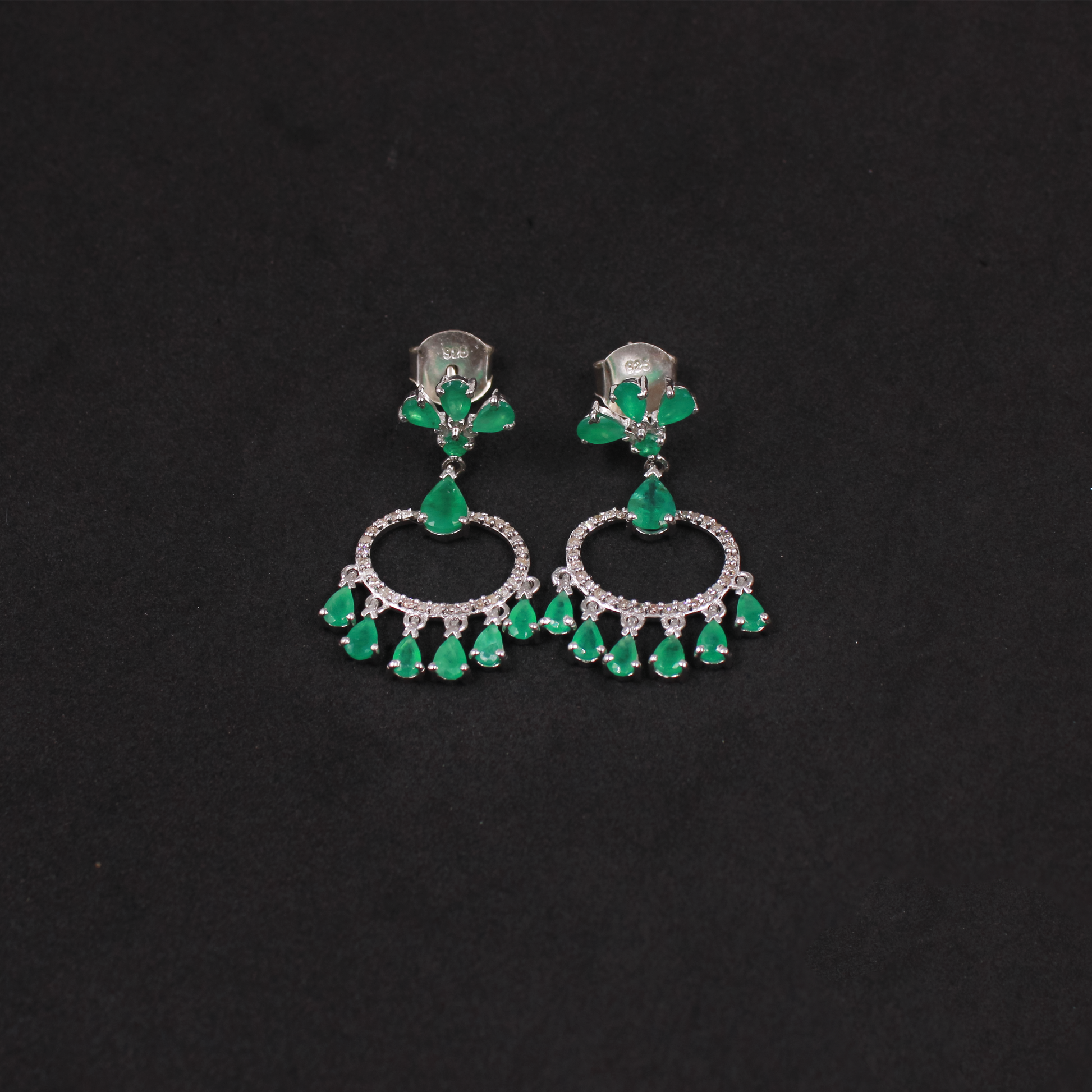Pair of earrings with green emerald gemstones on a black background