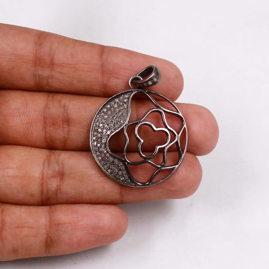 Silver pendant with heart design held between fingers on a white background