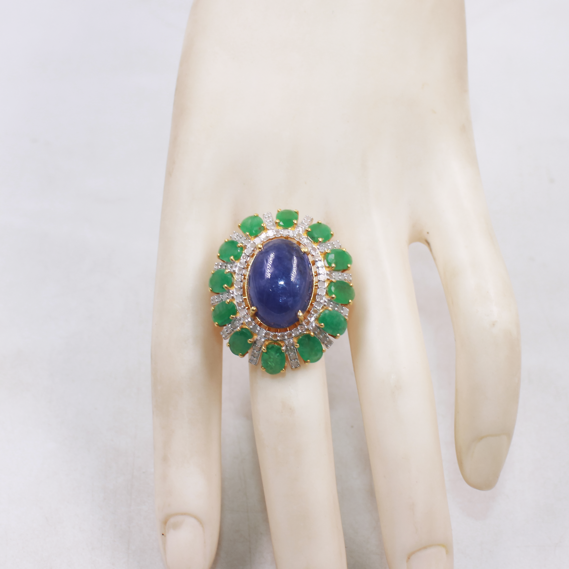 Oval blue kyanite cocktail ring with emerald and diamond halo