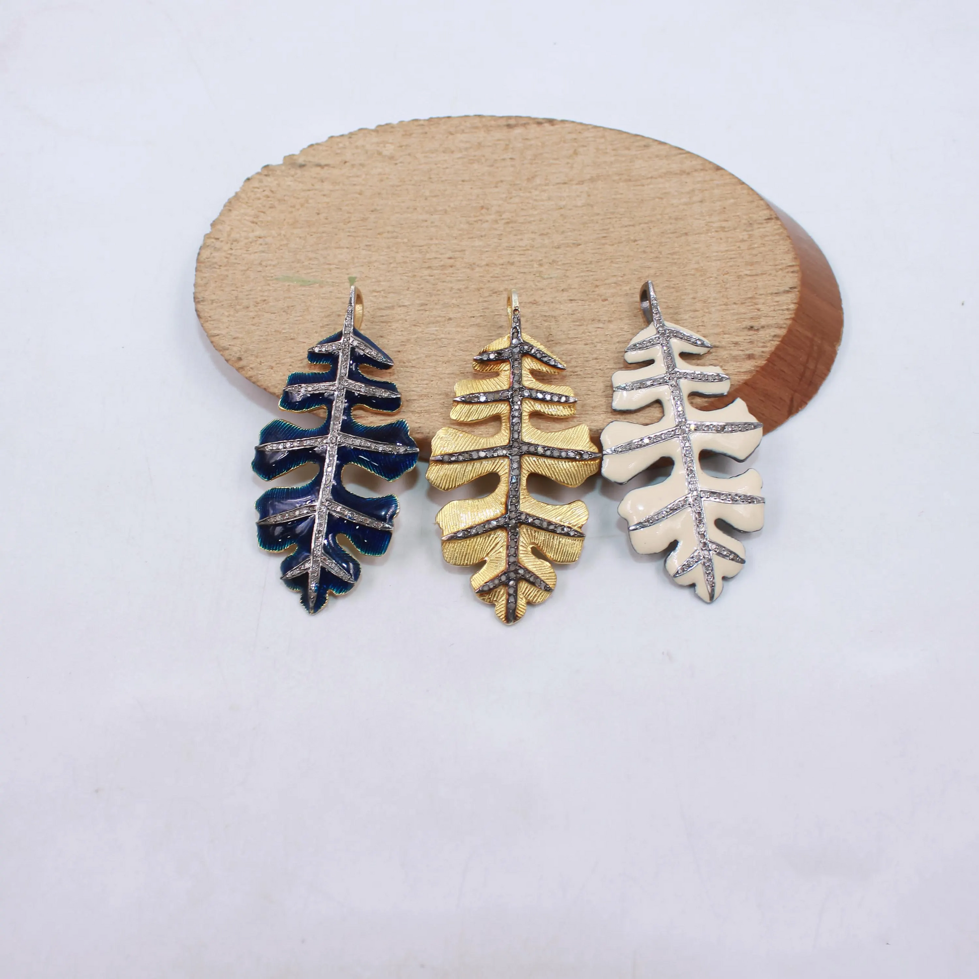 Three leaf-shaped earrings in blue, gold, and silver on a wooden stand with a white background.