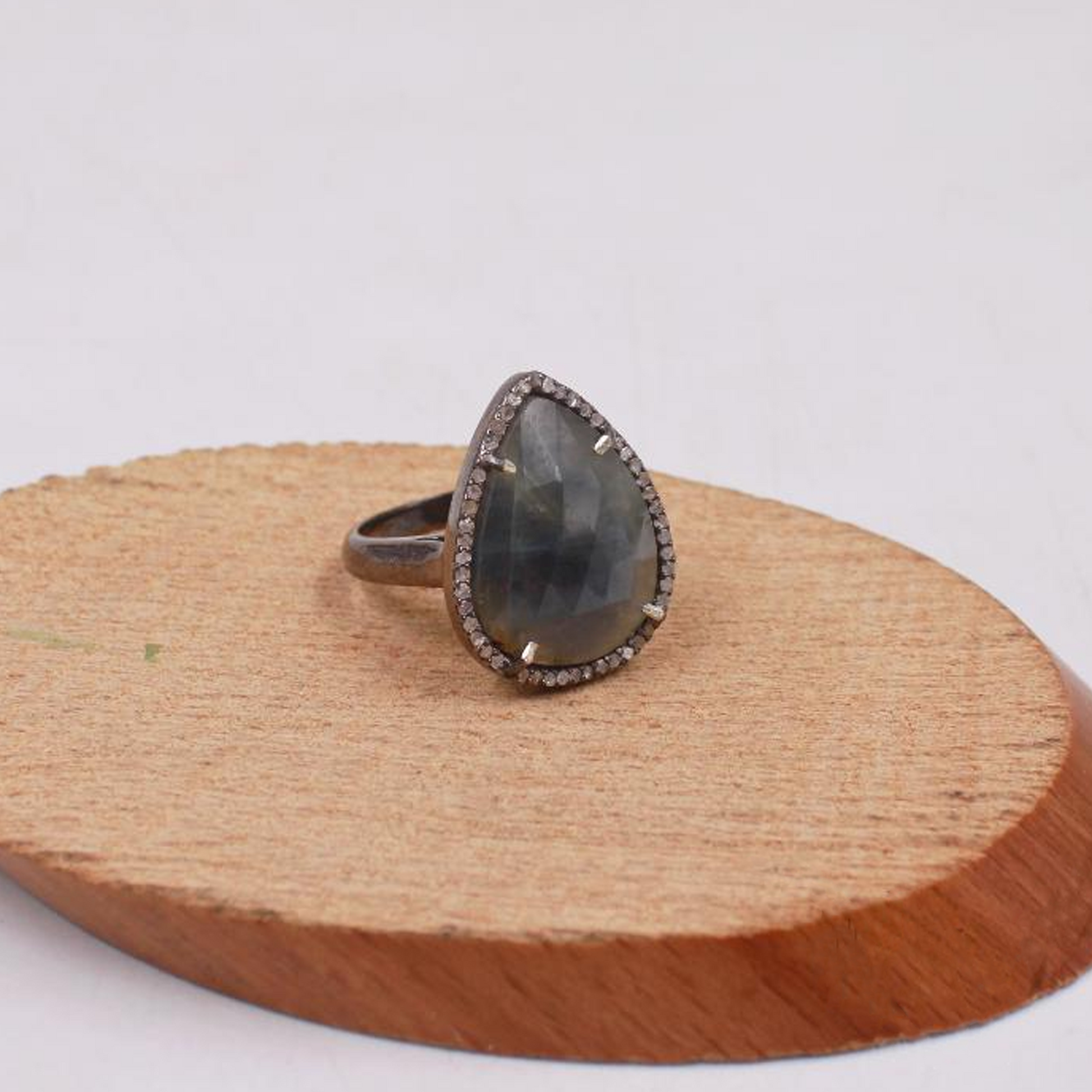 Teardrop-shaped ring with a gray stone on a wooden stand against a white background