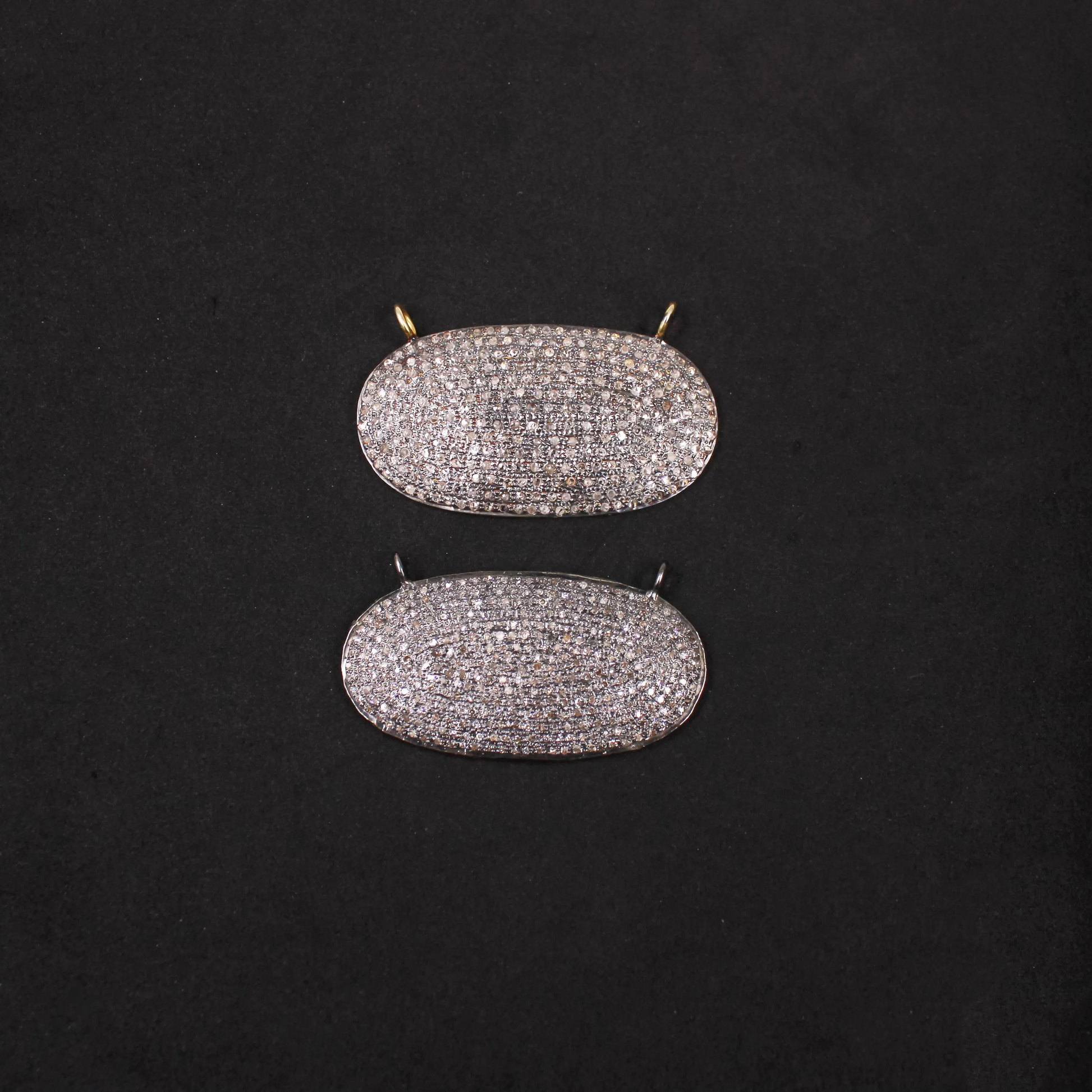 Pair of diamond-studded oval pendants on a black background