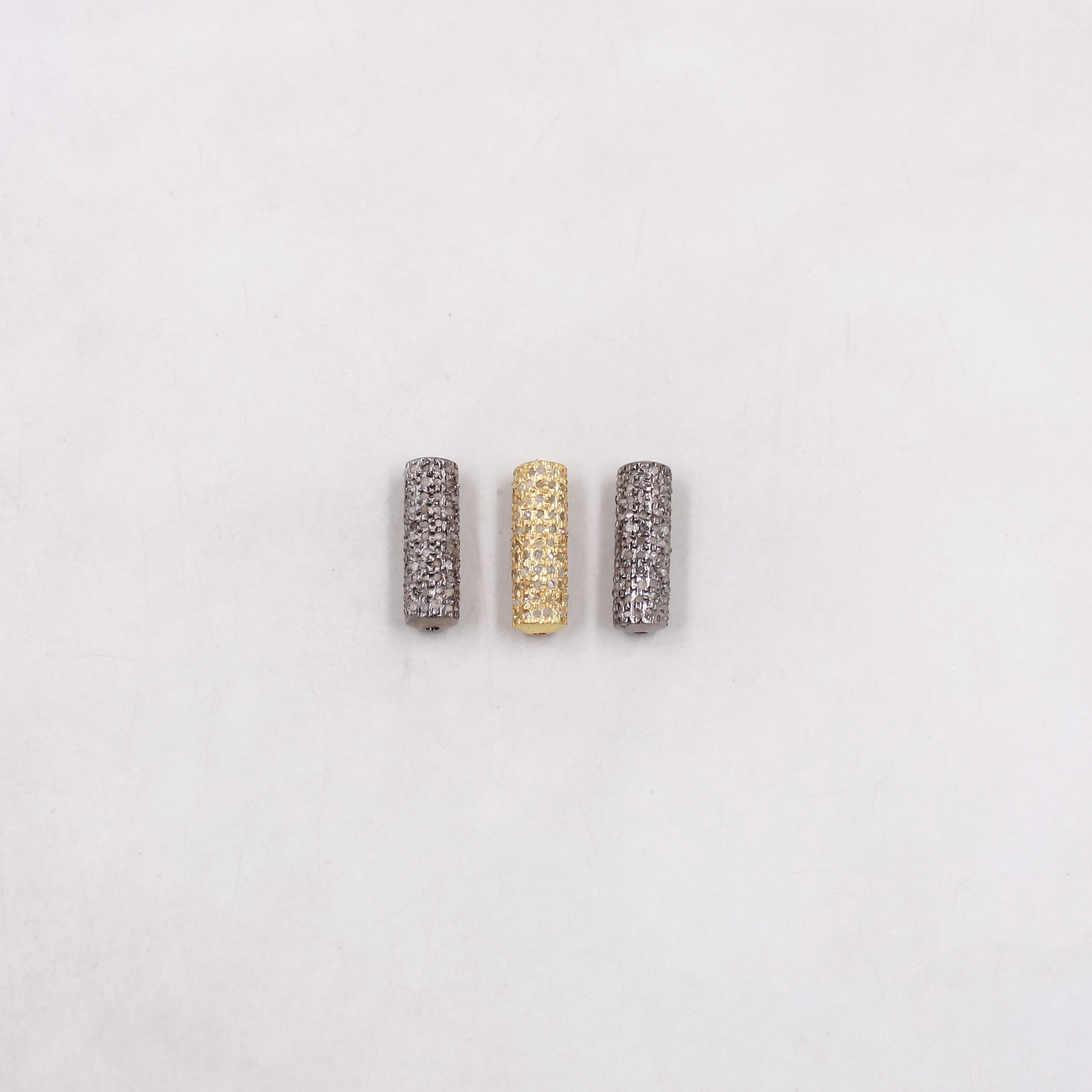 Three cylindrical beads in silver, gold, and gray on a light gray background