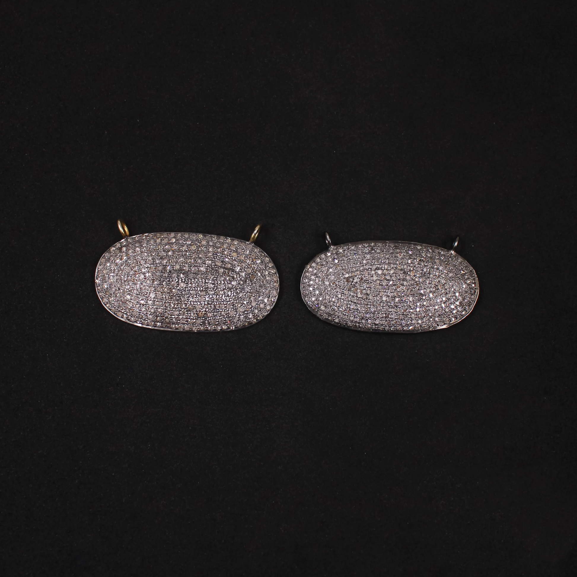 Pair of oval-shaped earrings with diamond-like stones on a black background