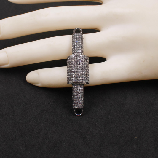 Silver cylindrical pendant on a mannequin hand against a black background
