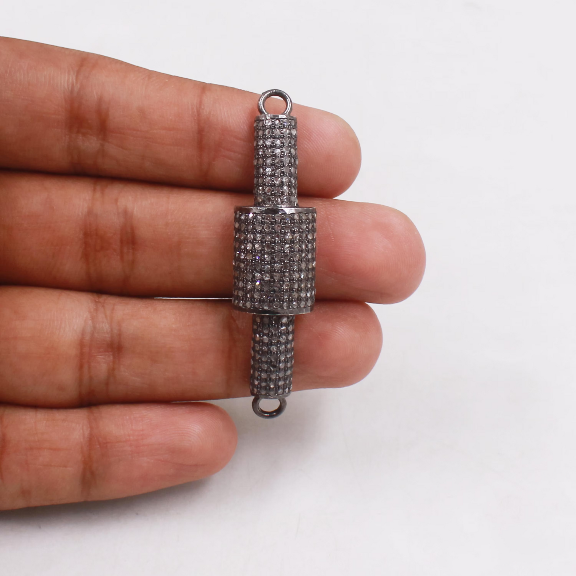 Silver microphone-shaped pendant held between fingers on a white background