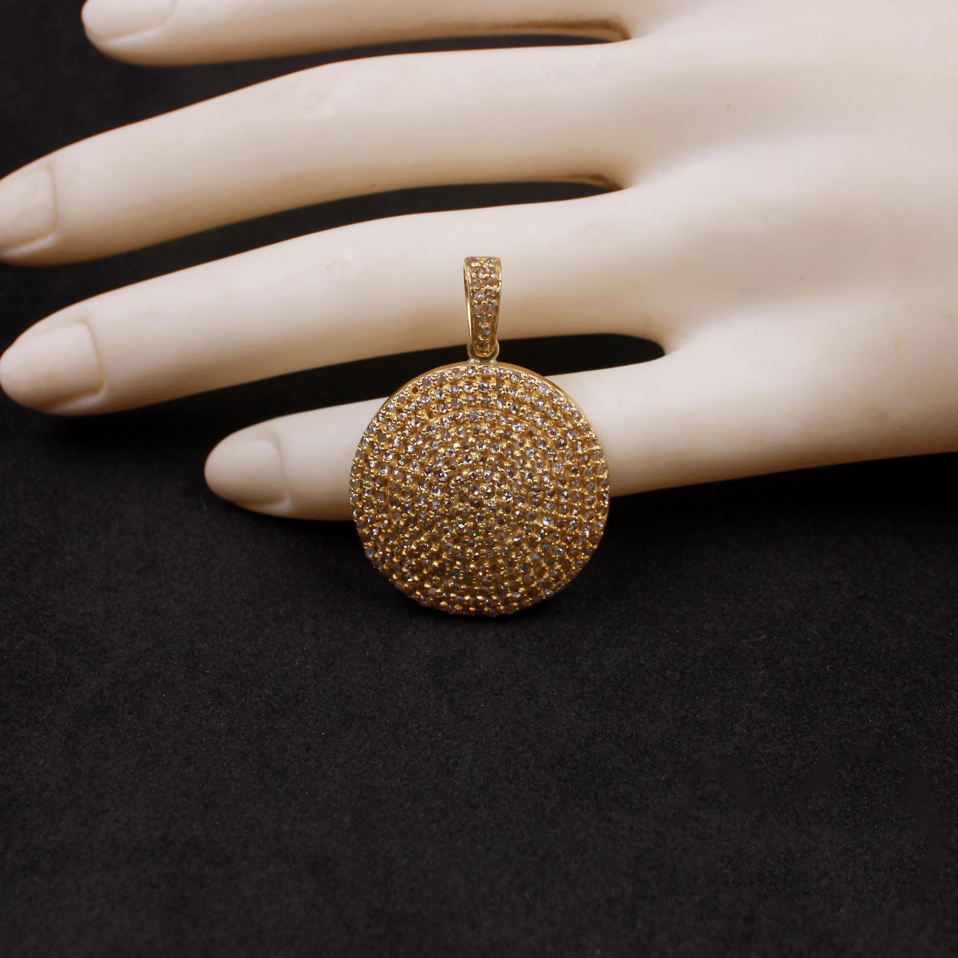 Gold pendant on a mannequin hand against a black background