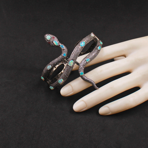 Decorative snake-shaped ring with turquoise stones on a mannequin hand against a black background
