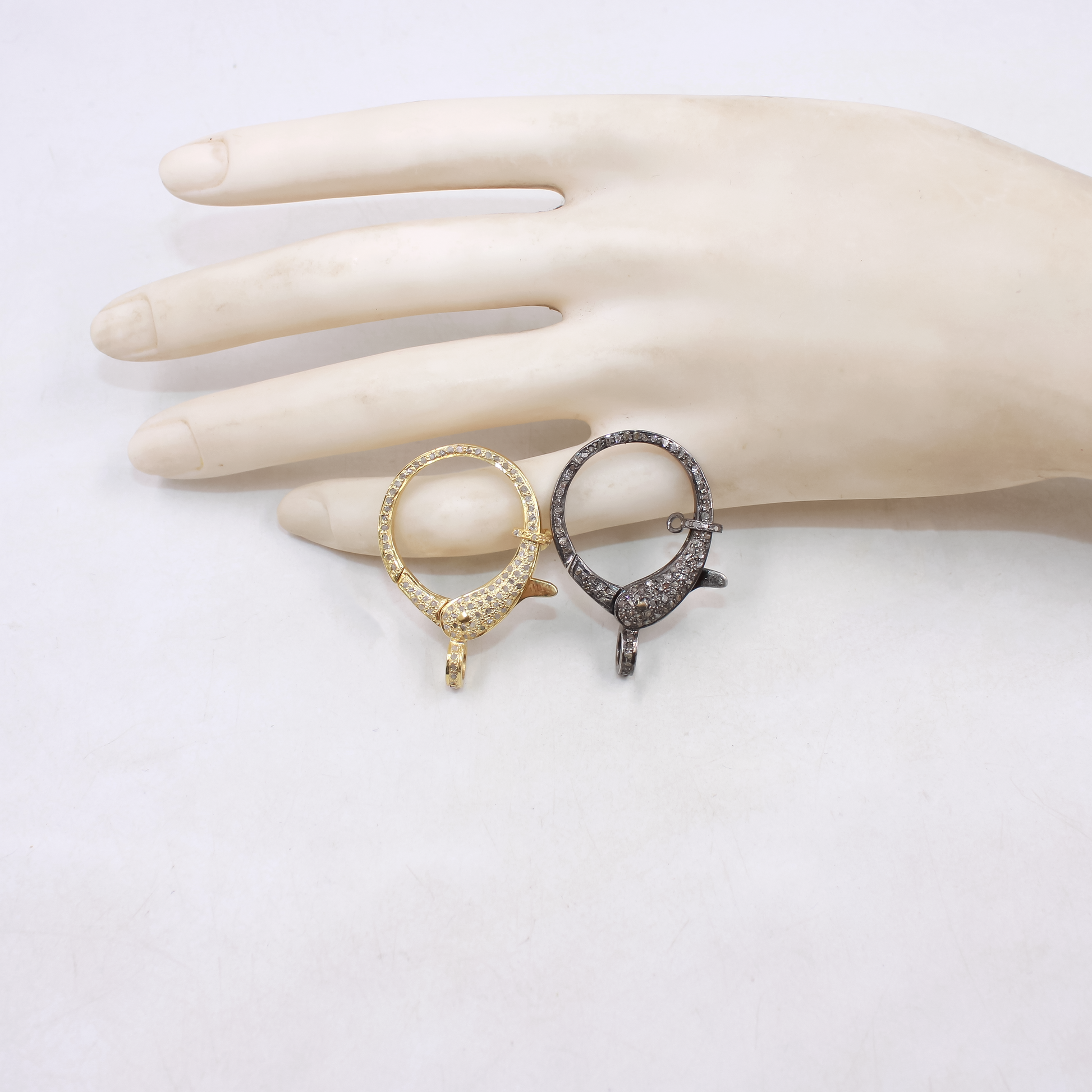 Two earrings, one gold and one black, on a mannequin hand against a white background.