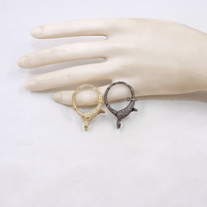 Two earrings, one gold and one black, on a mannequin hand against a white background.