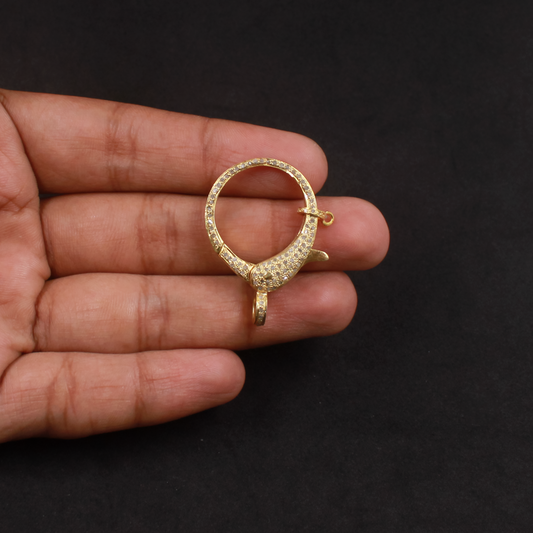 Gold jewelry piece held in a hand against a black background
