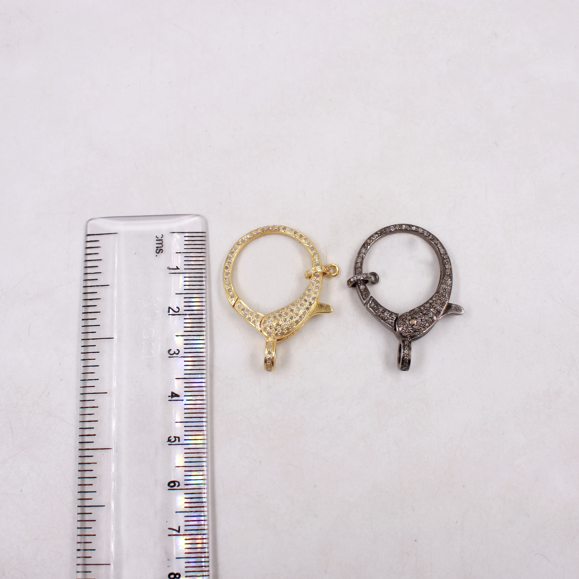 Two gold and silver jewelry clasps next to a ruler on a white background
