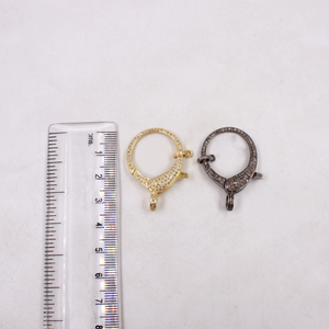 Two gold and silver jewelry clasps next to a ruler on a white background