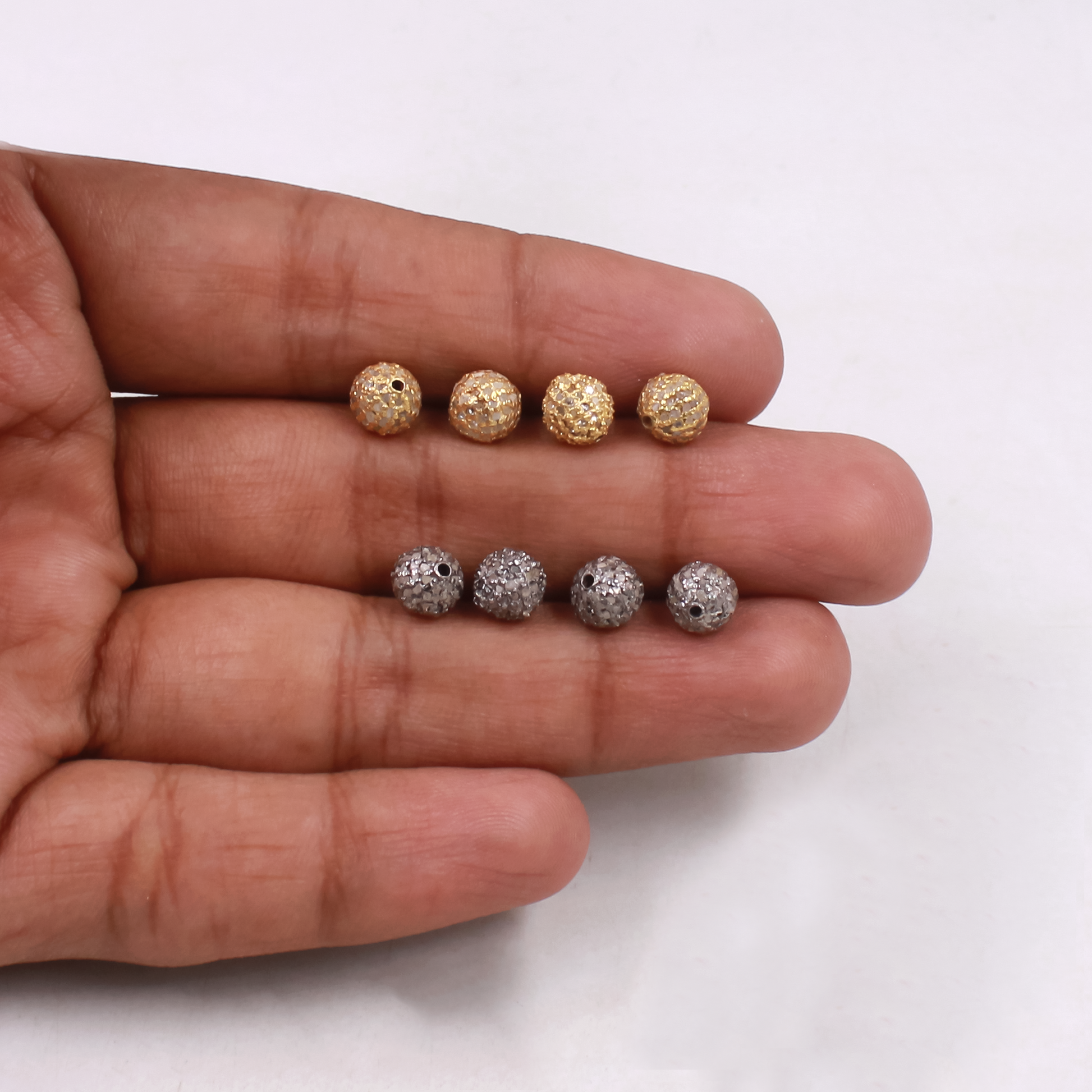Gold and silver beads on a hand against a white background