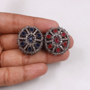 Beads with blue and red gemstones held between fingers on a white background