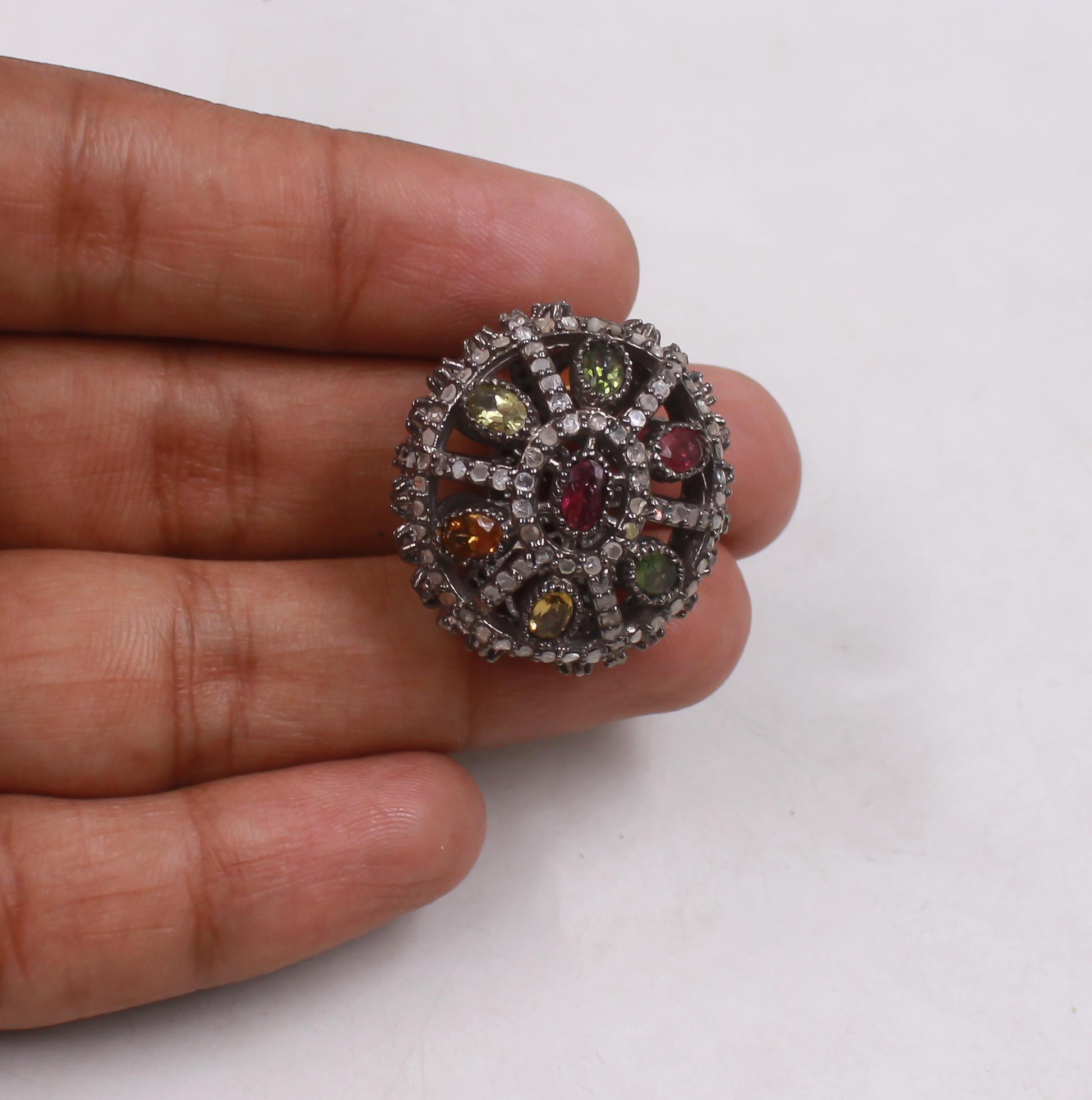 Close-up of a bead with multicolored gemstones held between fingers on a white background