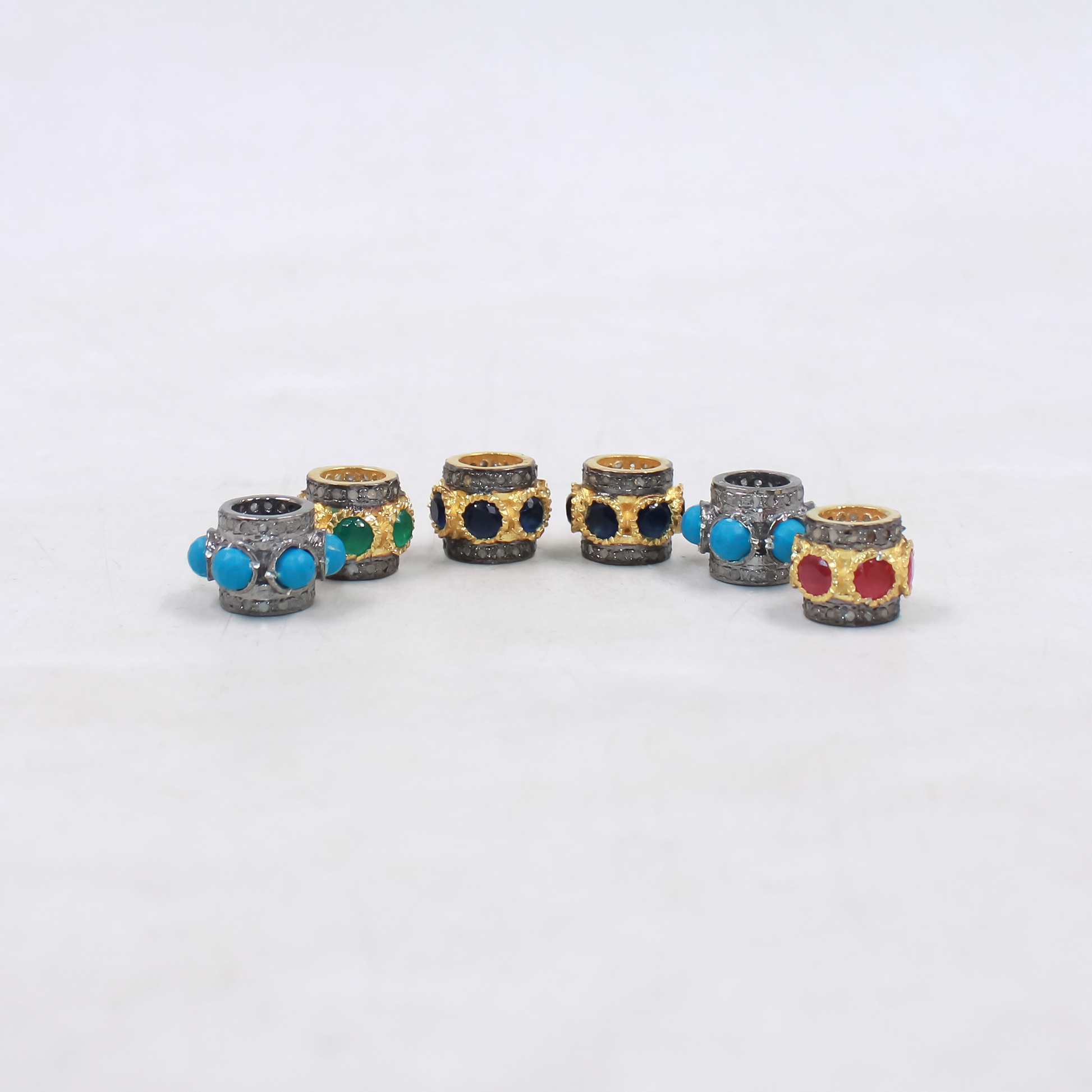 Set of six decorative cylindrical beads with colorful gemstones on a white background