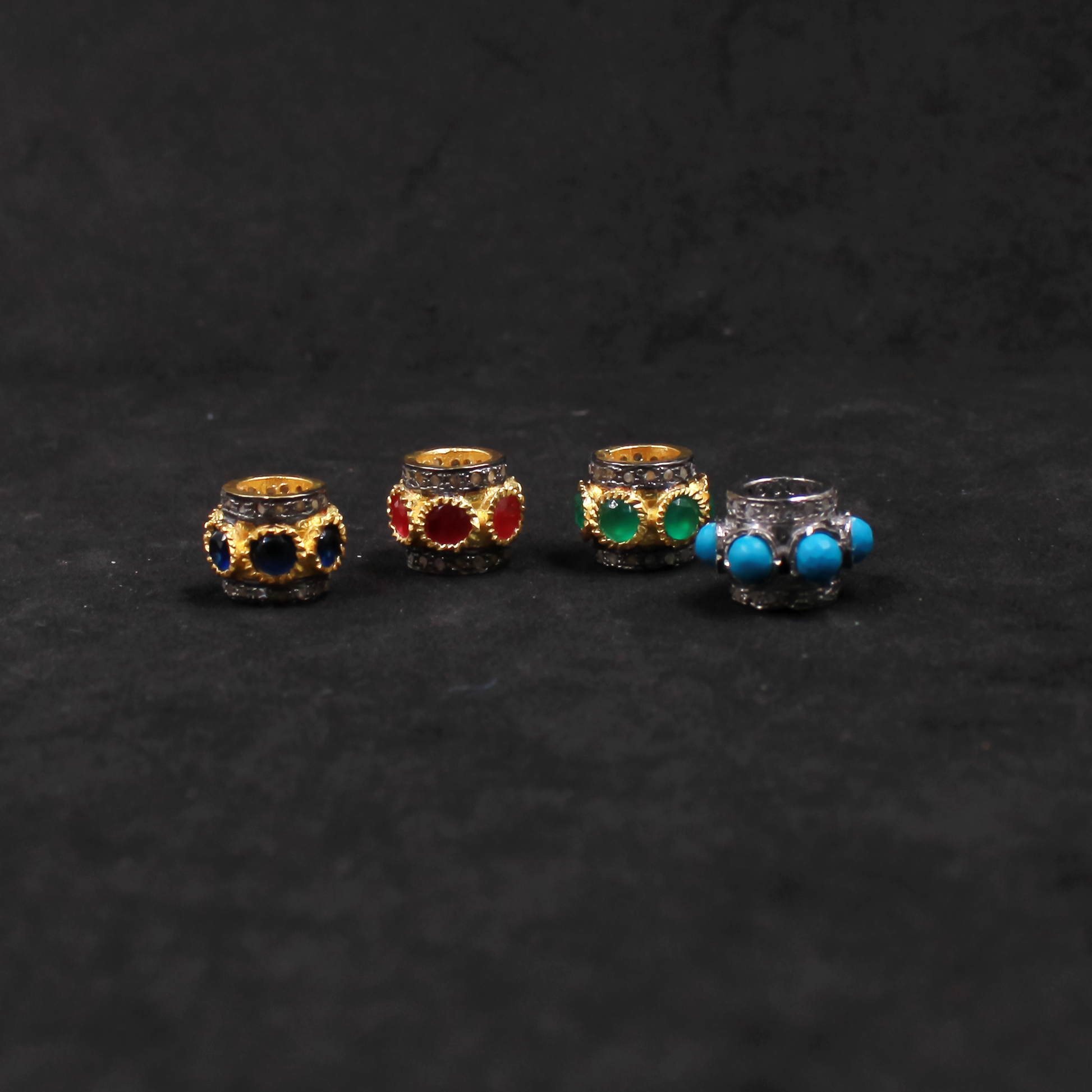 Four small jewelry items with colored stones on a dark textured background