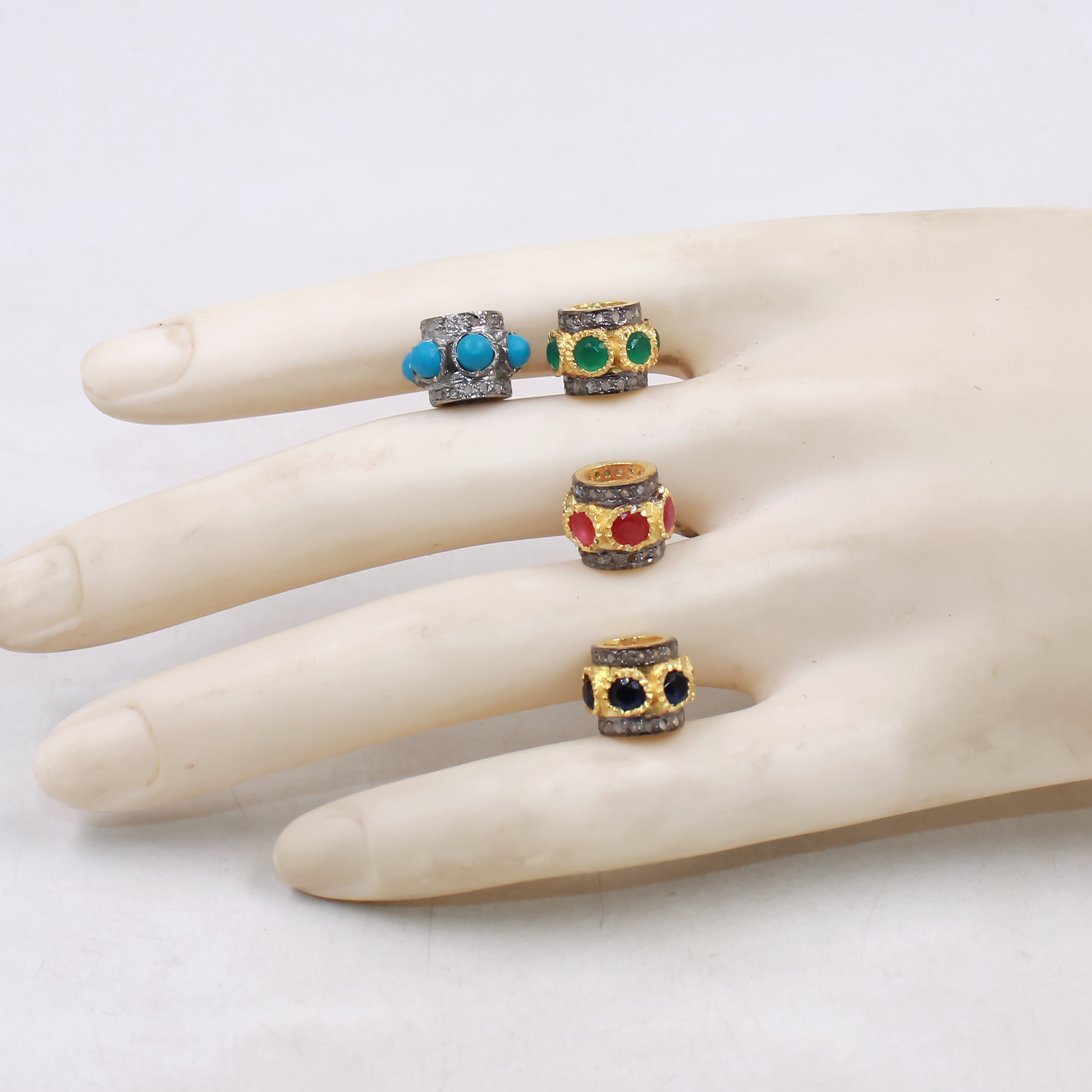 Four rings with colorful gemstones on a beads hand against a white background
