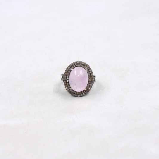 Ring with a pink gemstone and diamond-studded band on a white background