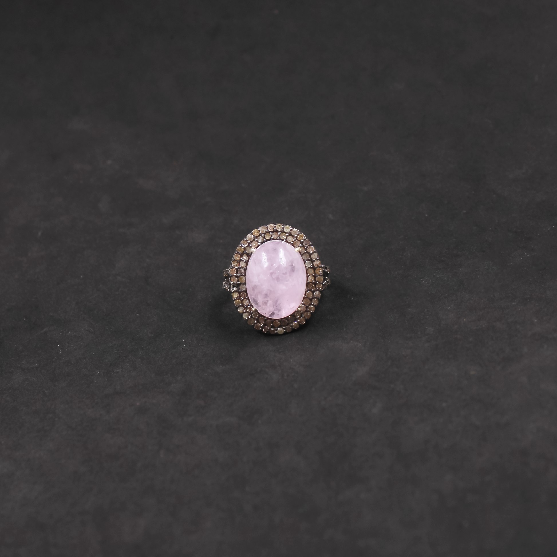 Ring with a pink gemstone and diamond-studded band on a dark gray background