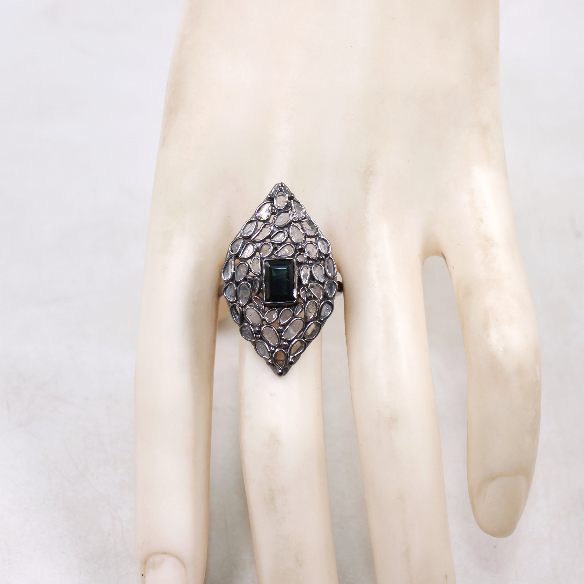 Ring with a diamond-shaped stone on a mannequin hand against a white background